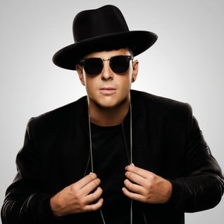 Timmy Trumpet in schwarzem Anzug vor grauem Hintergrund