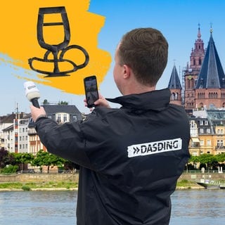 Ein Reporter mit Mikrofon, im Hintergrund ein Bild von Mainz und darüber Mainz aus Tape.