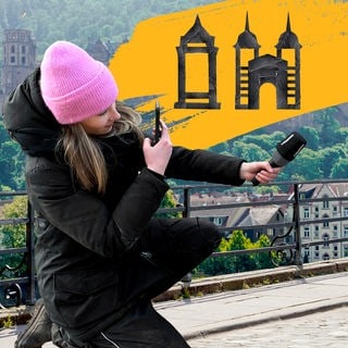 Eine Reporterin mit Mikrofon, im Hintergrund ein Bild von Heidelberg und darüber Mannheim-Heidelberg aus Tape.