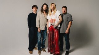 Die vier Bandmitglieder stehen vor einem grauen Hintergrund.