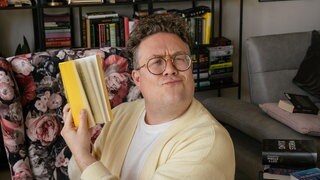 Thomas Bookclub hält ein Buch.